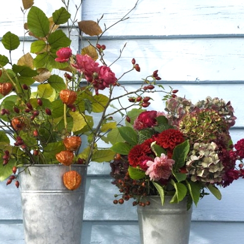 a duo of rustic Thanksgiving centerpieces in buckets, with bold fresh and dried blooms, greenery and seed pods is a very creative idea with a rustic feel