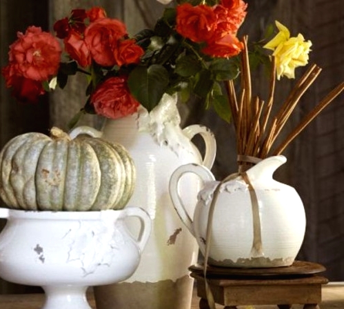 a shabby chic Thanksgiving centerpiece of jugs and bowls with red and yellow blooms and a pale green heirloom pumpkin