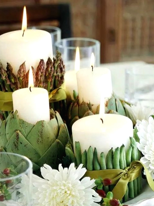 a neutral Thanksgiving centerpiece of pillar candles wrapped with fresh veggies and white blooms is a creative solution
