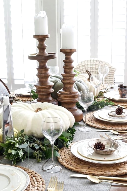 a pretty vintage rustic Thanksgiving centerpiece of eucalyptus, large heirloom pumpkins and white pillar candles in wooden candleholders