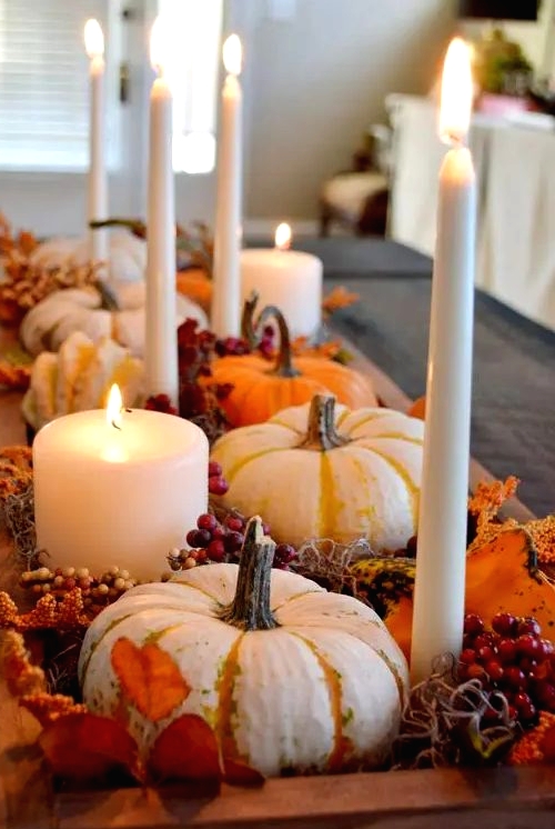 a rustic Thanksgiving centerpiece of a wooden box, berries, dried leaves, pillar and tall candles and some gourds is a cool idea