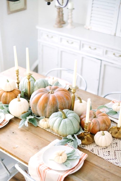 an all-natural Thanksgiving centerpiece of lots of fresh pumpkins stacked and some tall and thin candles in gilded candleholders