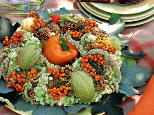 a pretty Thanksgiving centerpiece of a plate with greenery, berries, fruits and an orange pepper in the center is a creative all-natural idea