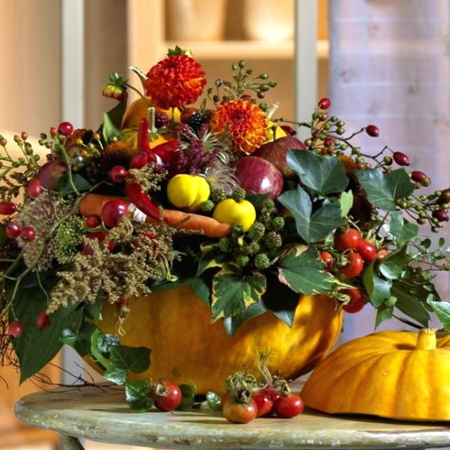 a super bold and all-natural Thanksgiving centerpiece with a bold pumpkin as a vase, lots of fresh veggies, berries, greenery and some brigth blooms is gorgeous