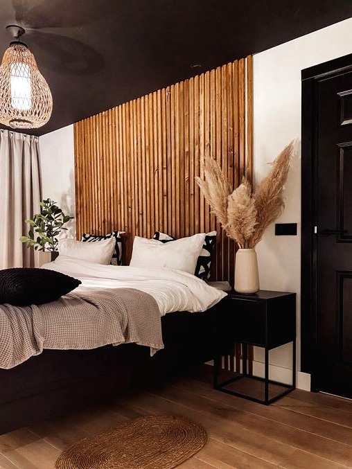 a chic and contrasting bedroom with a black ceiling, a wooden plank accent, a black floating bed and cool nightstands, a woven lamp and black and white bedding