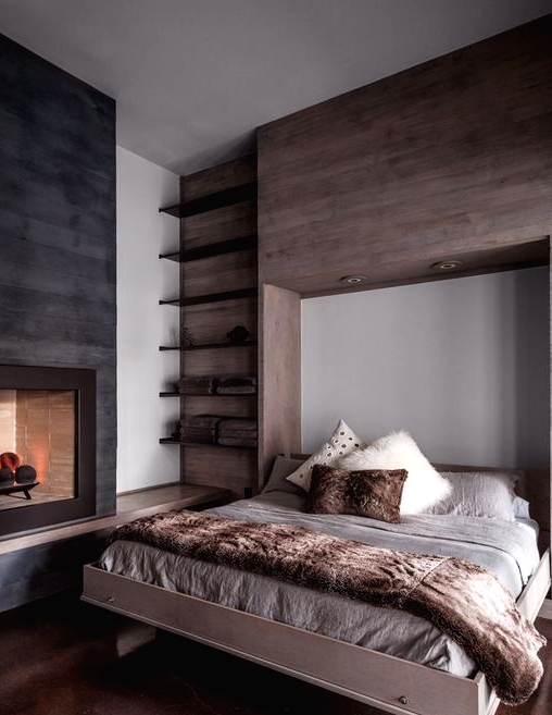 a cozy modern chalet bedroom with a floating bed, floating shelves, a fireplace and some faux fur bedding is very welcoming