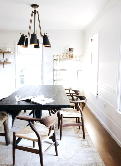 a light-filled dining space with a very dark-stained table that makes a statement, rich-stained chairs and a light-stained floor, a black pendant lamp and open shelves