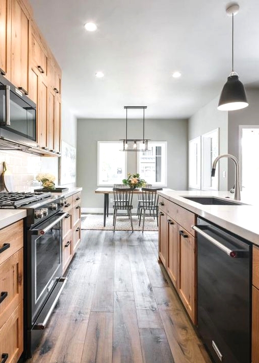 a modern farmhouse kitchen with light-stained cabinets, black built-in appliances and a dark reclaimed wood floor is amazing