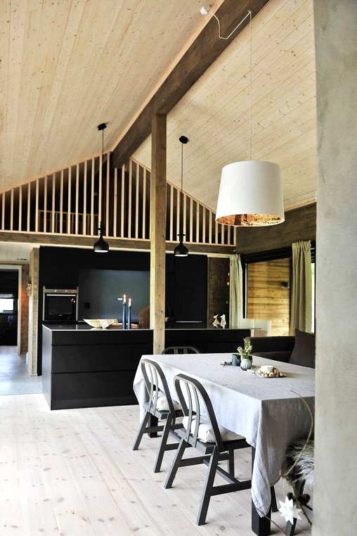 a Scandinavian kitchen with black cabinetry and a kitchen island, a whitewashed floor, a black table and chairs plus a light-stained ceiling