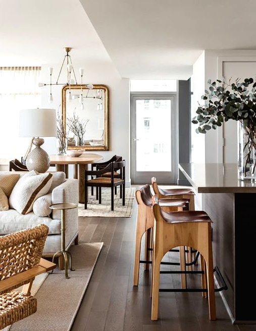 a stylish light-filled open layout with a welcoming bar space, living room and a dining zone, with varioys neutral wood tones and a dark wood floor and kitchen island