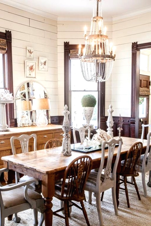 an eclectic dining room with dark-stained panels, a light-stained buffet, a rich-stained table and mismatching chairs plus a crystal chandelier