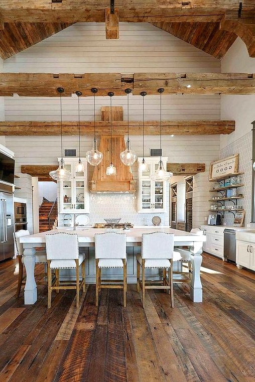 a white farmhouse kitchen with white cabinets, a refined kitchen island, a reclaimed wooden floor, light-stained wooden beams and a ceiling