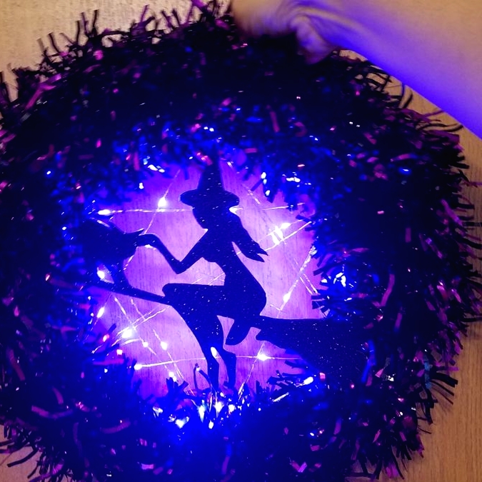a purple Halloween wreath with purple lights and a witch on the broom silhouette is a fun and cool decoration
