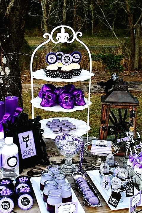 a black and purple Halloween sweets table with various desserts, candies and cupcakes, with purple glitter skull decor