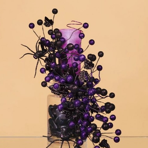 a purple candle held by blakc and purple berries and black spiders for easy and fun Halloween decor