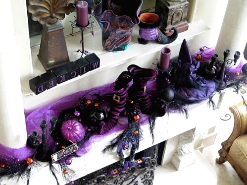 a bold purple and black Halloween mantel with pumpkins, witches' legs and hats, candles, berries on branches and much other stuff