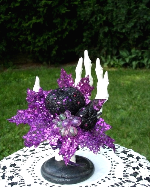 a bold Halloween decoration of a skeleton hand holding a purple sequin leaf, pumpkins and rhinestone grapes is a gorgeous idea to rock