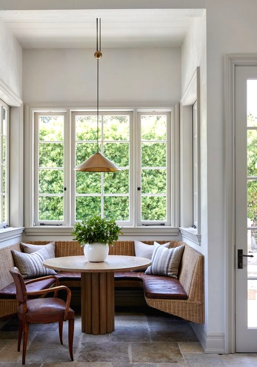 a cozy dining space with large French windows, a woven floating seating, a wooden round rable, a pendant lamp is amazing