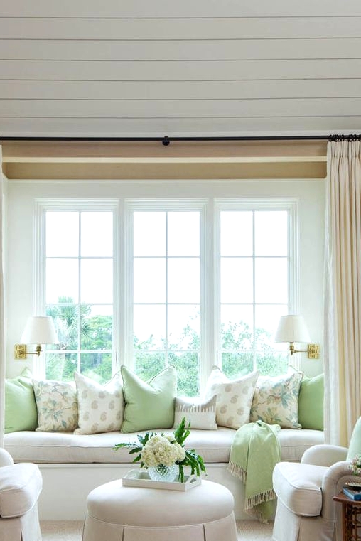 a large French window with a cozy windowsill sofa styled with lots of pillows that is a lovely alternative to a usual sofa in the living room