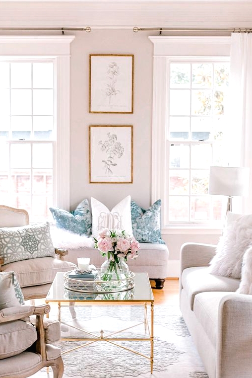 a pretty and welcoming neutral living room with tall French windows, refined vintage furniture, a glass coffee table and printed pillows