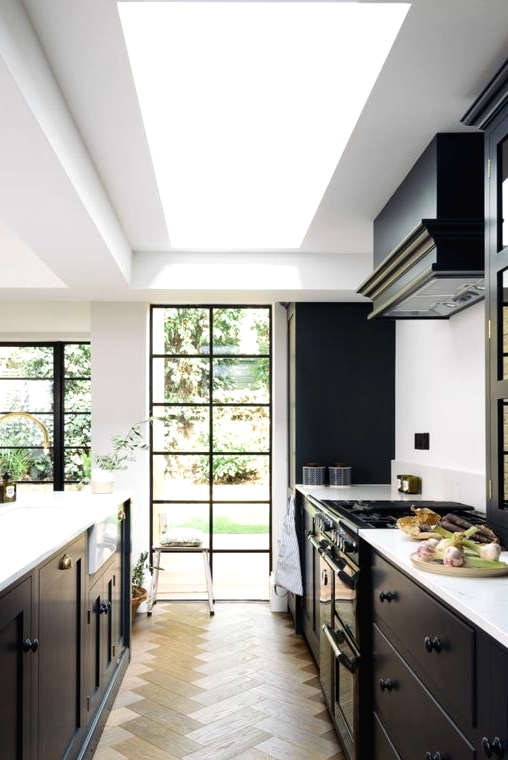 a stylish modern black kitchen with a large skylight and French windows with black frames, a black hood and a parquet floor