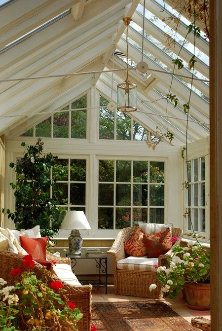 a vintage-inspired rustic sunroom with French windows and whole walls, a glass slated roof, potted blooms and a tree and colorful touches