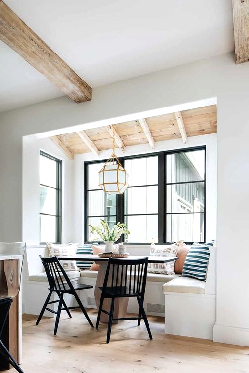 several black windows, a built-in seating in the niche, a large table, a faceted pendant lamp and vintage black chairs