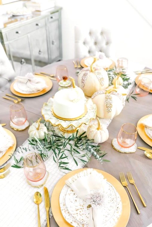 a beautiful glam Thanksgiving table setting with a striped runner and speckled plates, gold cutlery and glam embellished pumpkins plus greenery