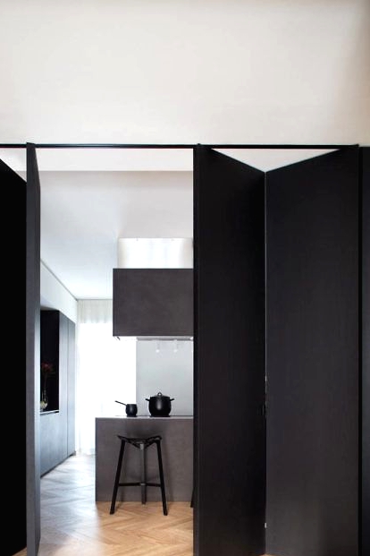 a black folding door matches the minimalist space and the color palette and makes a bold statement in the house