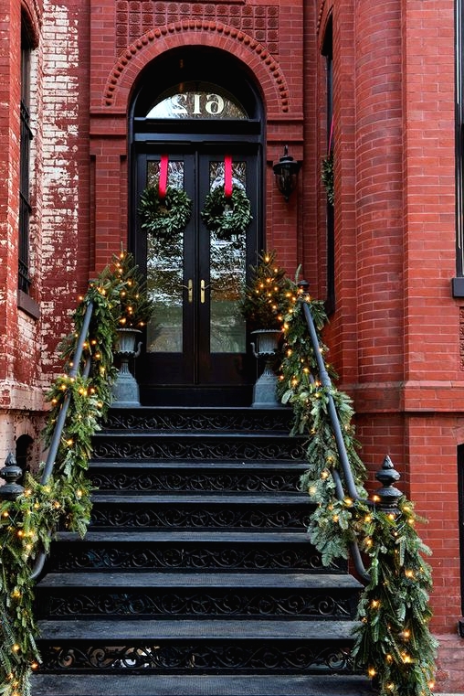 a beautiful festive porch with evergreen garlands and lights, mini Christmas trees and wreaths with red ribbons is amazing