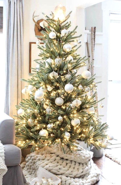 a fantastic Christmas tree with lights and white and silver ornaments plus a white chunky knit tree skirt is gorgeous