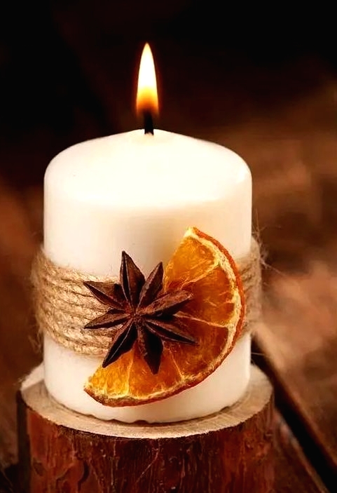 a candle with twine, a dried fruit slice and a spice piece is a gorgeous idea for fall or winter and it provides cool aroma