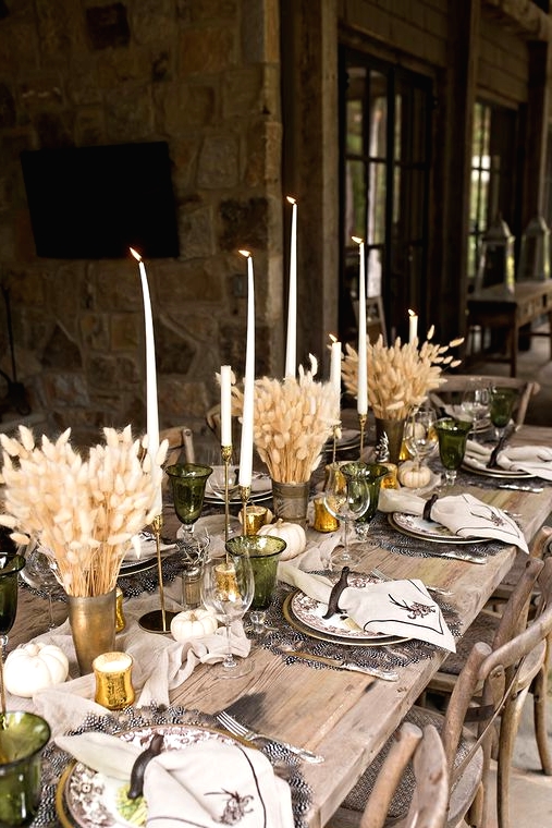 a gorgeous rustic Thanksgiving tablescape with feather placemats, bunny tail centerpieces, tall and thin candles, printed plates and napkins