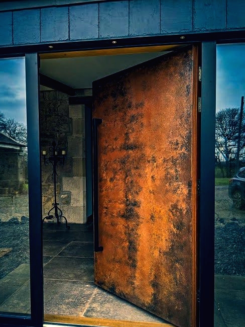 a unique weathered oversized metal front door with an oversized handle is a fantastic solution with an unusual color scheme
