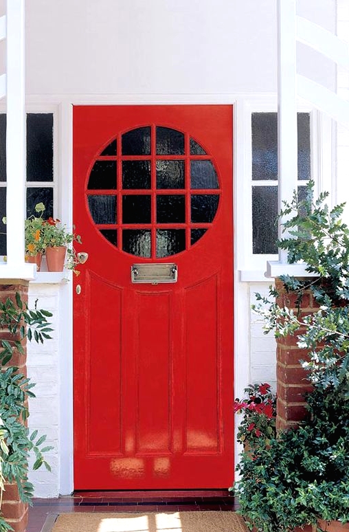 a hot red front door with glass panes and refined metal touches, with greenery and bold red blooms that echo with the door