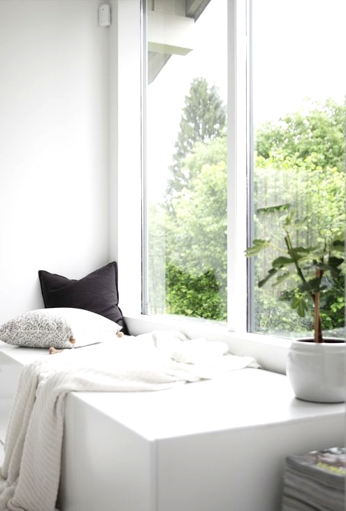 a minimalist space with a double-height window and a storage daybed built-in, with pillows and a blanket is a cool and stylish idea
