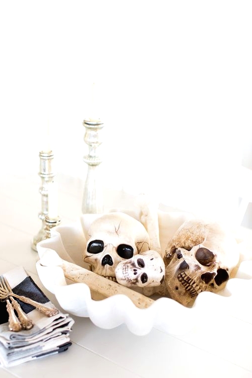 pretty white Halloween decor with a white bowl with skulls and bones, silver candleholders and white candles in them