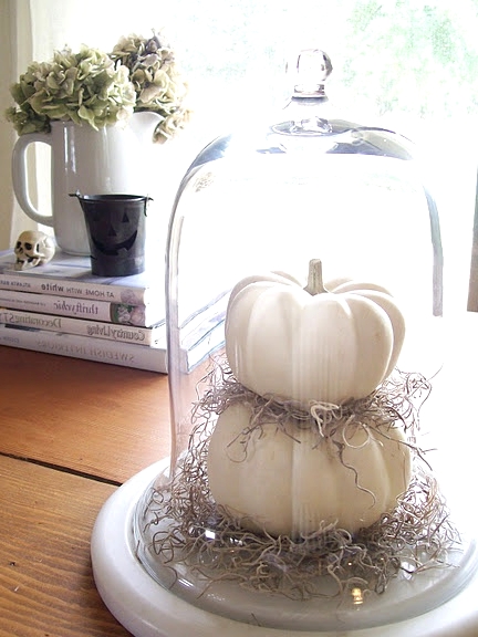 a large cloche with hay and stacked pumpkins is a cool idea to style your space for Halloween and it doesn't require any effort