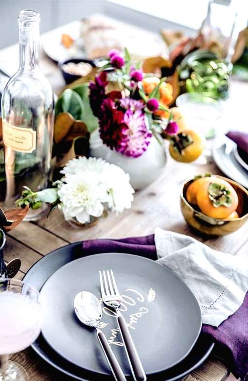 a laid-back and rustic Thanksgiving tablescape with greenery, bold purple blooms, fruits, black plates and purple napkins