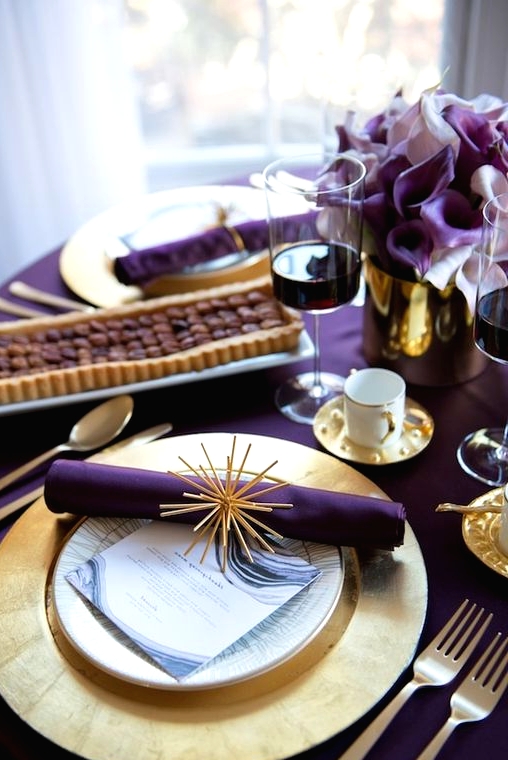 a modern glam Thanksgiving tablescape with a purple tablecloth, napkins and callas, gold charrgers and cutlery and a vase