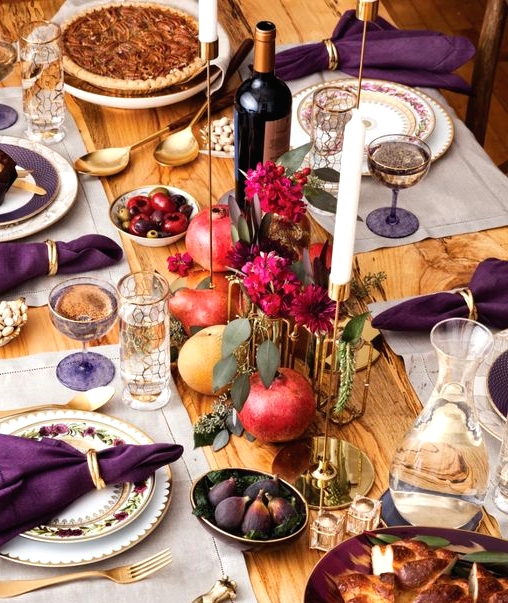 a refined Thanksgiving tablescape with neutral placemats, purple napkins, bold fuchsia blooms, gold touches and berries