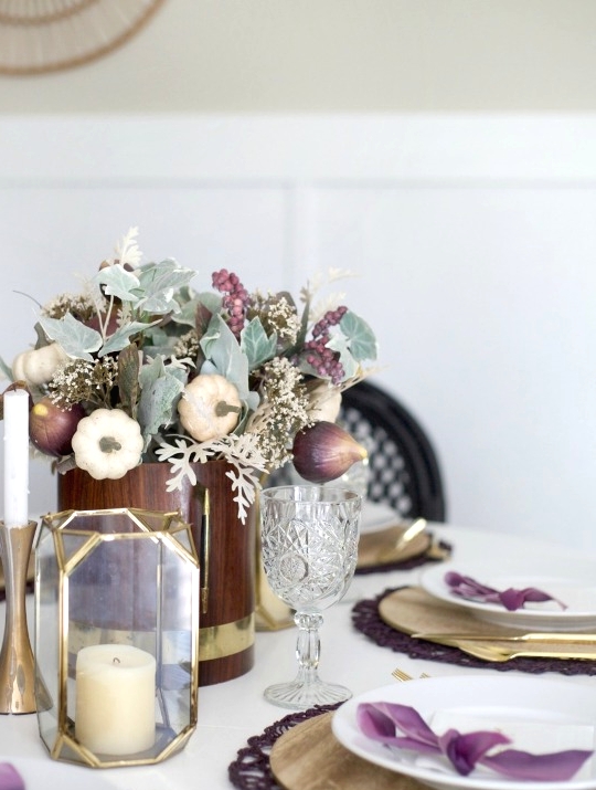 a Thanksgiving table setting with plywood placemats and a gold faceted candleholder, purple placemats and bows, purple veggies and berries