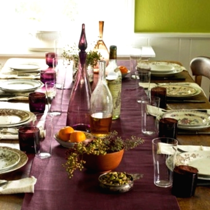 a purple Thanksgiving tablescape with a purple runner and glasses, botanical plates, greenery and fruits is cool