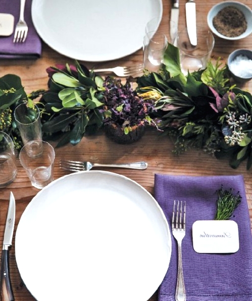 a chic Thanksgiving tablescape with a greenery runner, purple napkins and berries, white porcelain and chic cutlery is amazing