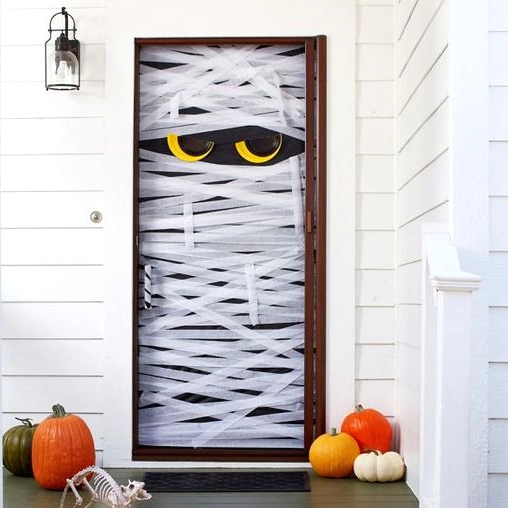 a simple Halloween front door styled as a mummy with eyes, with colorful pumpkins and a cat skeleton is a fun and easy DIY idea
