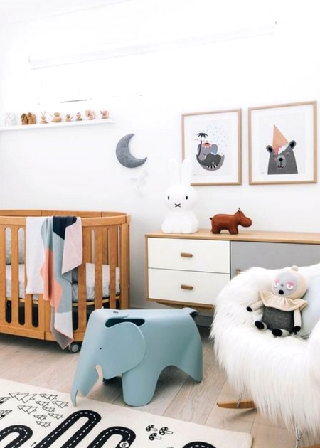 a cozy Scandi nursery with a stained crib, a stained dresser, a faux fur chair, a blue elephant chair, some artworks and a play rug