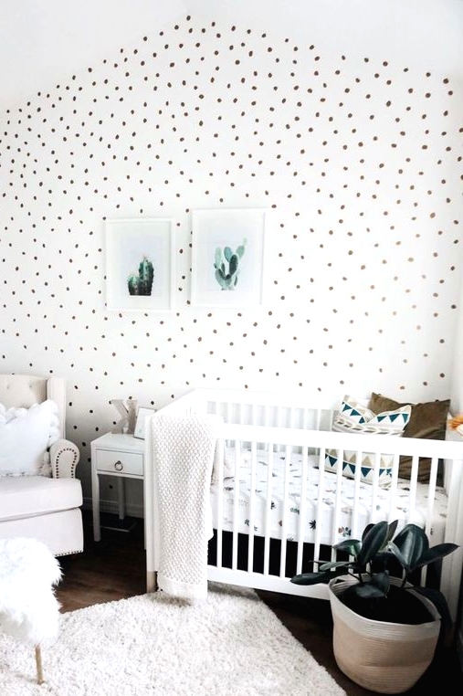 a fresh neutral nursery with a spotted accent wall, white and creamy furniture, a neutral rug and bedding, a mini gallery wall
