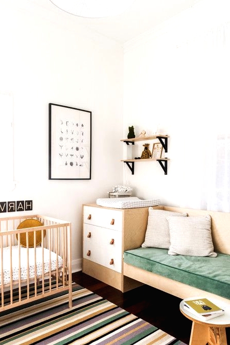 a Nordic chic nursery with white and stained furniture, a built-in sofa, a brigth striped rug, open shelves and a printed pouf