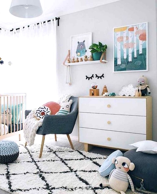 a Scandi nursery with bright touches - artworks, pillows, a pouf and a chair and some bright bedding in the crib is lovely