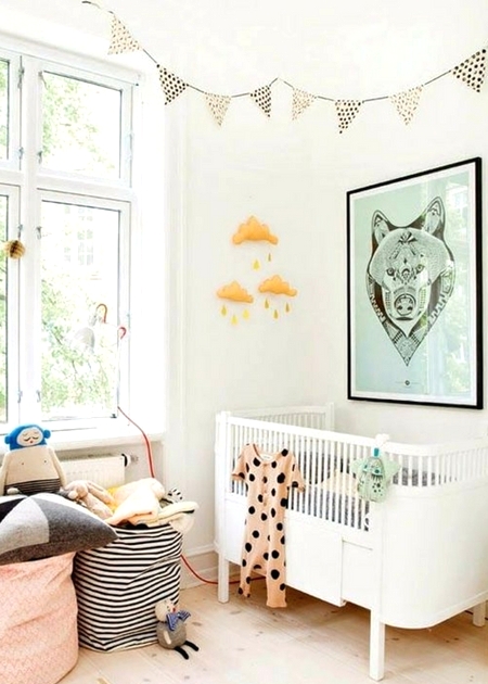 a Scandinavian nursery with a white crib, a green artwork, printed bunting, printed baskets with pillows and toys and a mobile